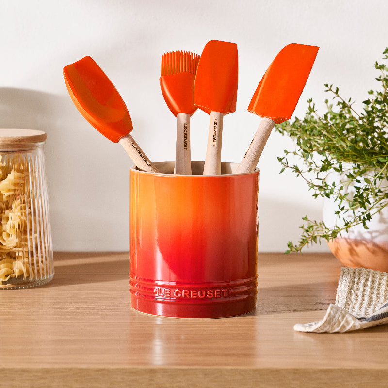Set of orange silicone spatulas in a red container on a wooden surface with a blurred background.