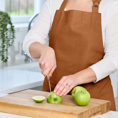 Person in a brown apron cutting green apples on a wooden cutting board in a kitchen.