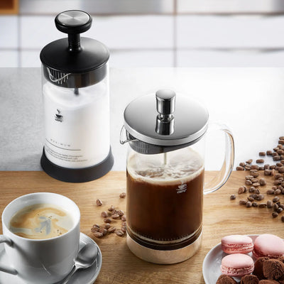 French press coffee maker with a cup of coffee, coffee beans, and pastries on a wooden surface.