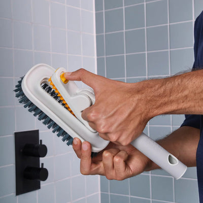Person using a scrubber to clean a tiled bathroom wall.