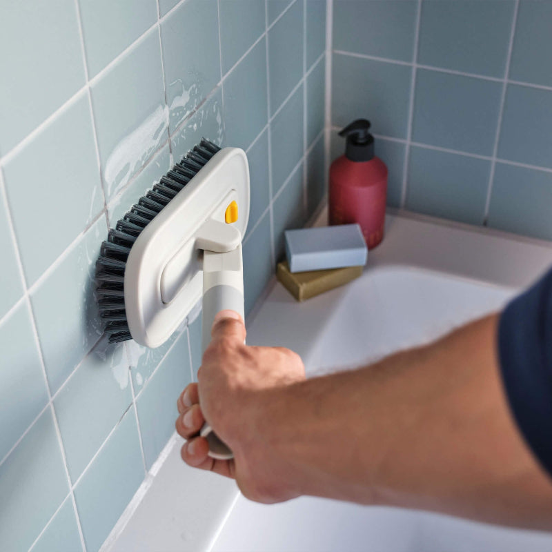 Person cleaning a bathtub with a brush against tiled walls.