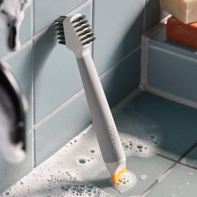 Gray toothbrush with orange bristle tip on a tiled bathroom floor