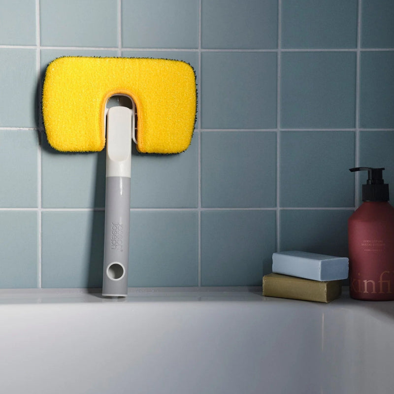 Cleaning tool with yellow sponge head on a tiled bathroom wall