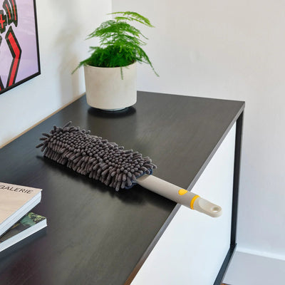 Duster on a desk with a plant and books in the background