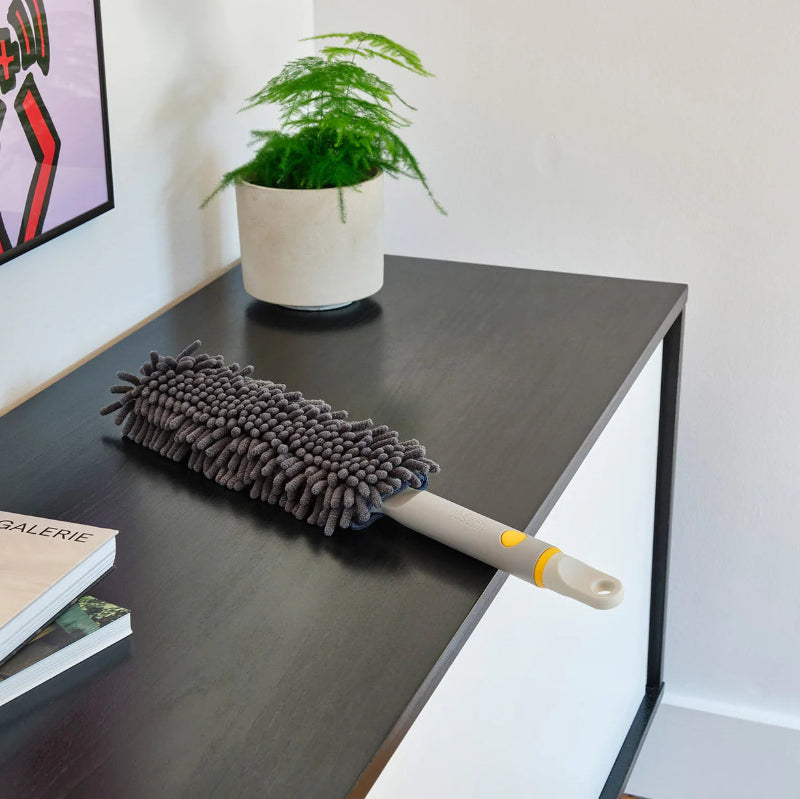 Duster on a desk with a plant and books in the background