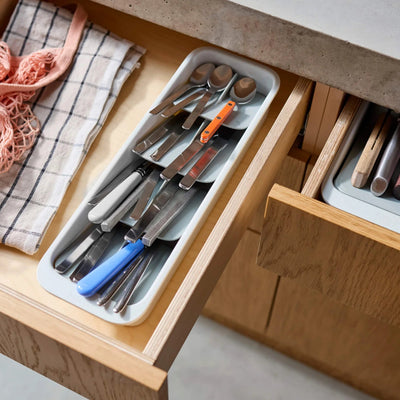Wooden drawer with cutlery and kitchen tools on a light background