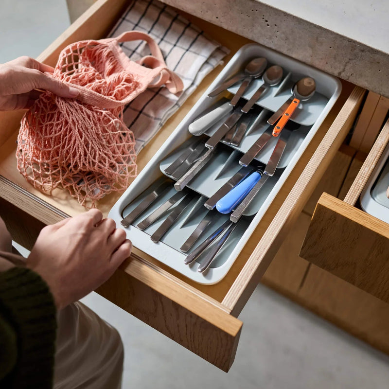 Open drawer with utensils and a person holding a pink mesh bag.