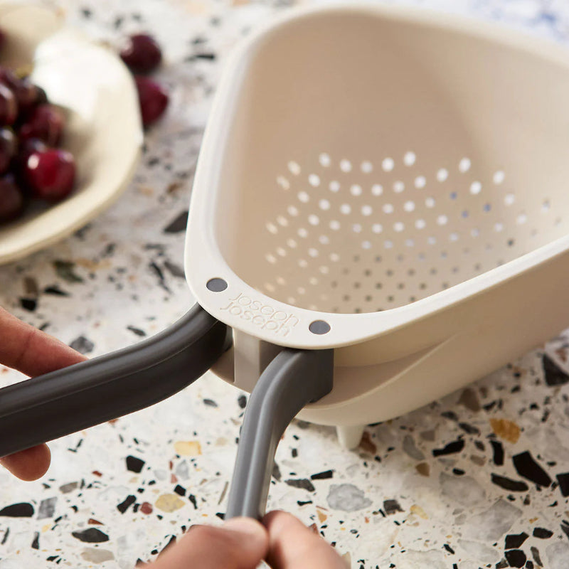 Hand using a kitchen strainer over a bowl on a speckled countertop.
