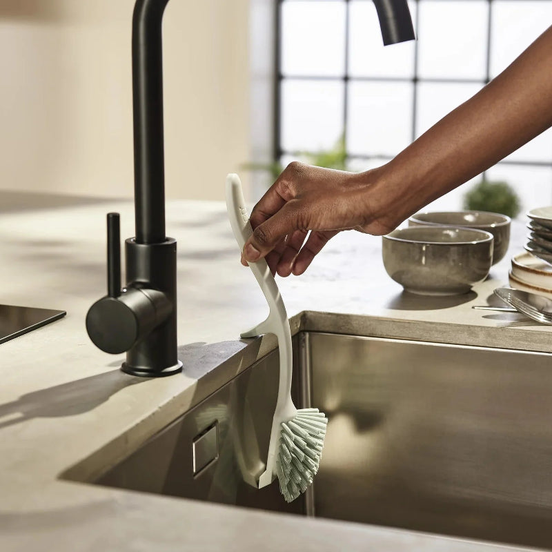 Person using a scrubber to clean a kitchen sink with a modern faucet.