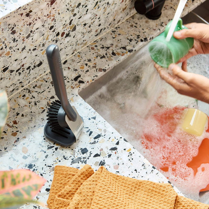 Person washing a green sponge over a sink with soapy water, on a speckled countertop.