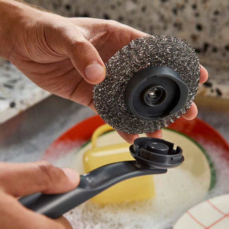 Person holding a scrubber with a black handle over a kitchen sink.