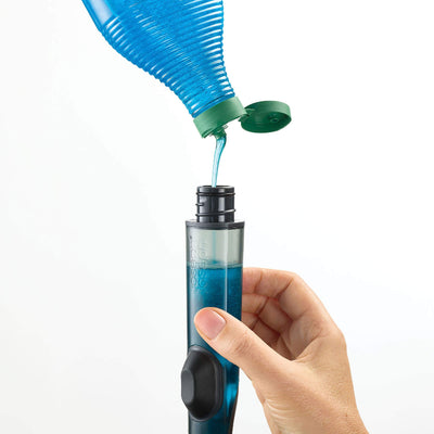 Hand holding a blue liquid being poured into a clear container with a white background