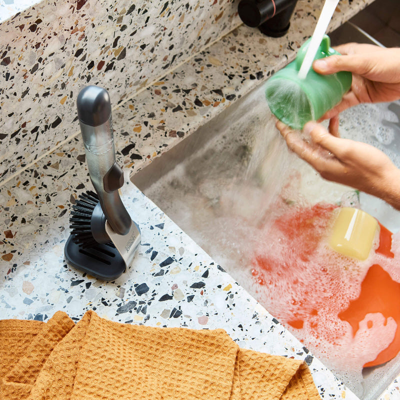 Person using a green silicone bottle brush to clean a sink with soap and water.