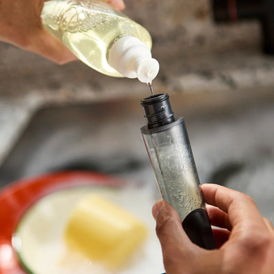 Person pouring a liquid from a bottle into another container with a blurred background