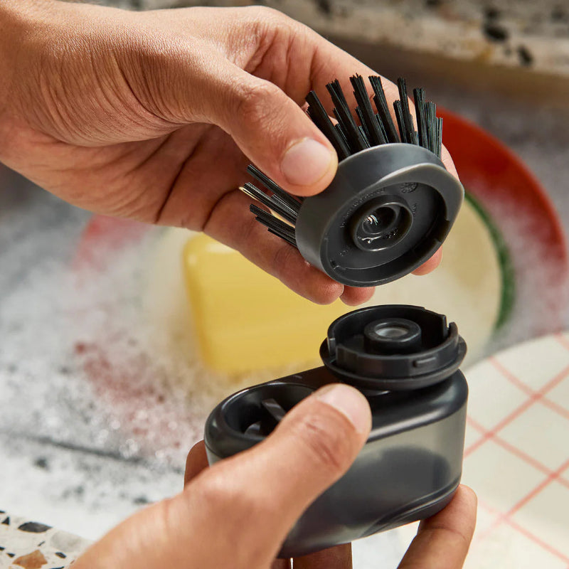 Person holding a black kitchen brush with bristles over a sink.