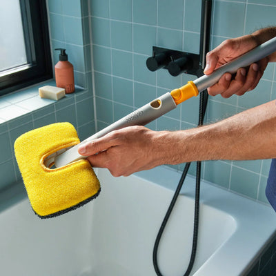 Person cleaning a bathtub with a yellow scrubber and gray handle.