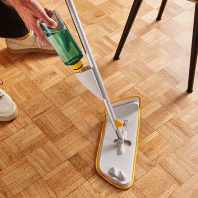 Person cleaning a wooden floor with a mop and green cleaning solution.