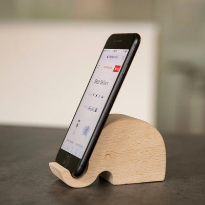 Wooden elephant phone stand holding a smartphone on a gray surface with a blurred background