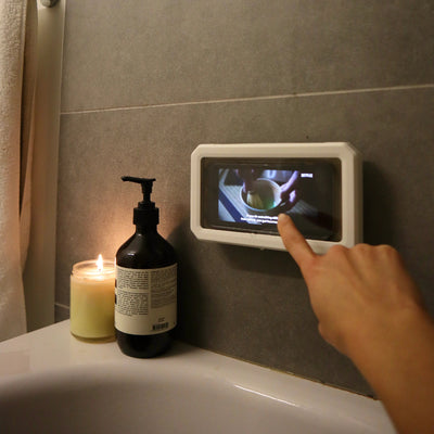 Hand using a digital display on a bathroom wall next to a candle and soap dispenser.