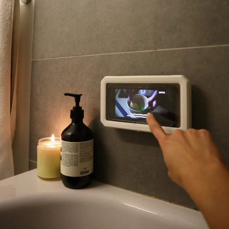 Hand using a digital display on a bathroom wall next to a candle and soap dispenser.