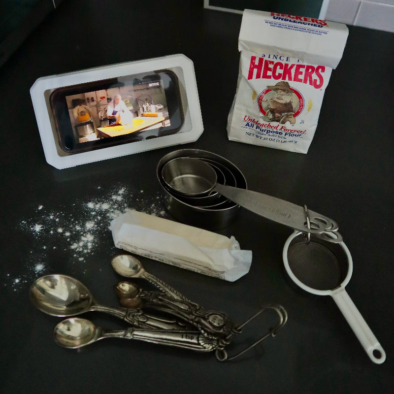 Baking ingredients and utensils on a dark surface with a smartphone displaying a recipe.