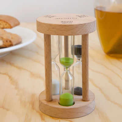 Wooden hourglass timer on a wooden surface with cookies and a cup in the background