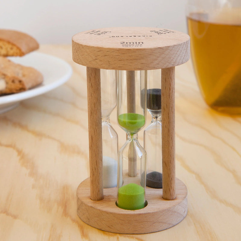 Wooden hourglass timer on a wooden surface with cookies and a cup in the background