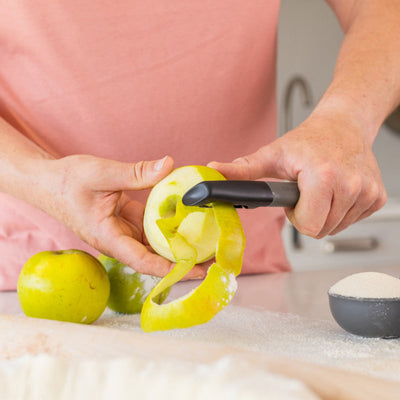 Person using a yellow kitchen tool on green apples in a kitchen setting.