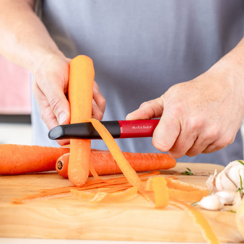 Person using a carrot peeler on carrots on a wooden cutting board.