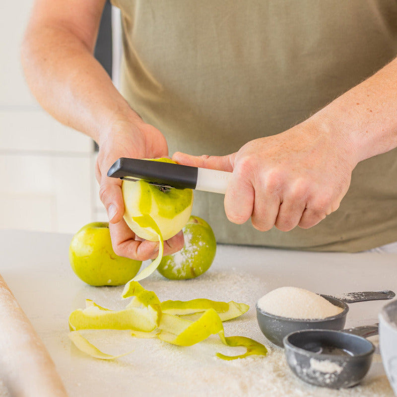 Person peeling apples with a peeler on a kitchen counter.