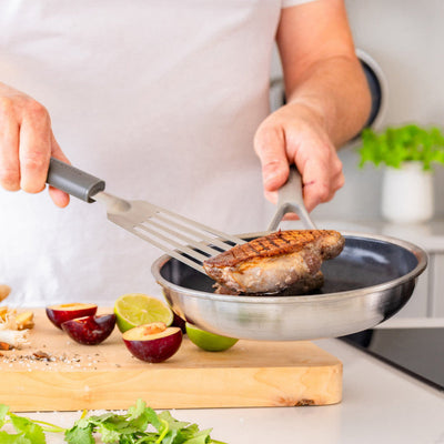 Person cooking on a stove with a pan and spatula, surrounded by ingredients on a cutting board.