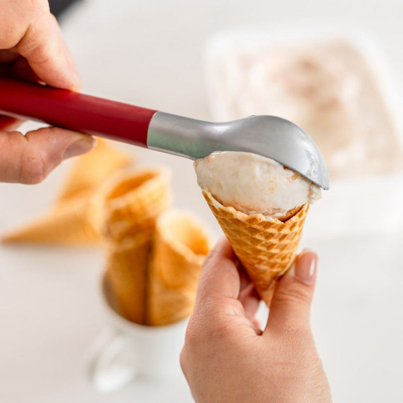 Person scooping ice cream into a waffle cone with a red-handled scoop.