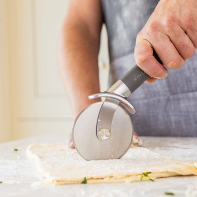 Person using a pizza cutter on dough with a blurred kitchen background