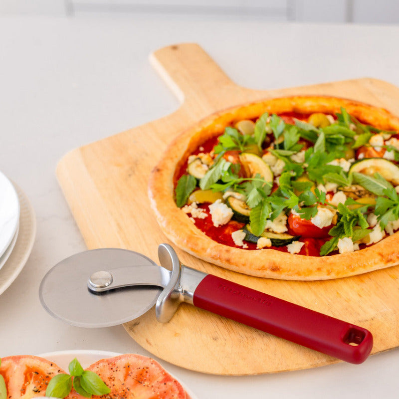 Vegetable pizza on a wooden board with a pizza cutter, on a white surface.