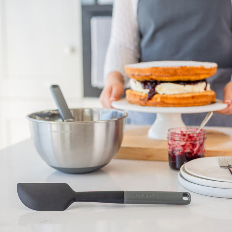 Person holding a cake with a bowl, spatula, and plates on a kitchen counter.