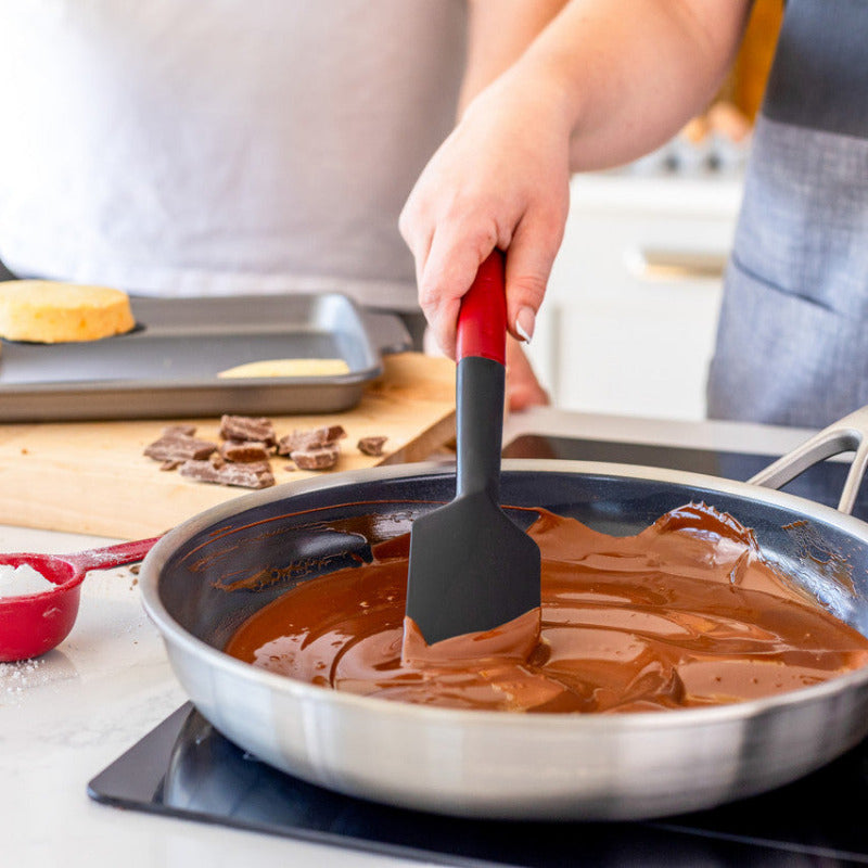Person cooking chocolate in a pan with a spatula, surrounded by baking ingredients.