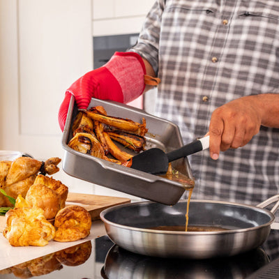 Person cooking in a kitchen with roasted vegetables and bread on a tray.