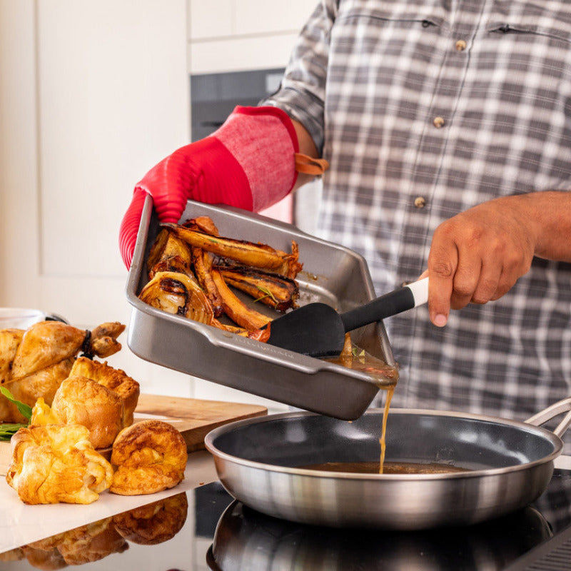 Person cooking in a kitchen with roasted vegetables and bread on a tray.