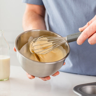 Person whisking batter in a bowl with a bottle of milk and baking tray in the background