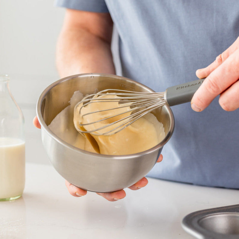 Person whisking batter in a bowl with a bottle of milk and baking tray in the background