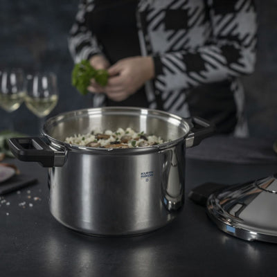 Stainless steel pot on a table with ingredients and a person in the background