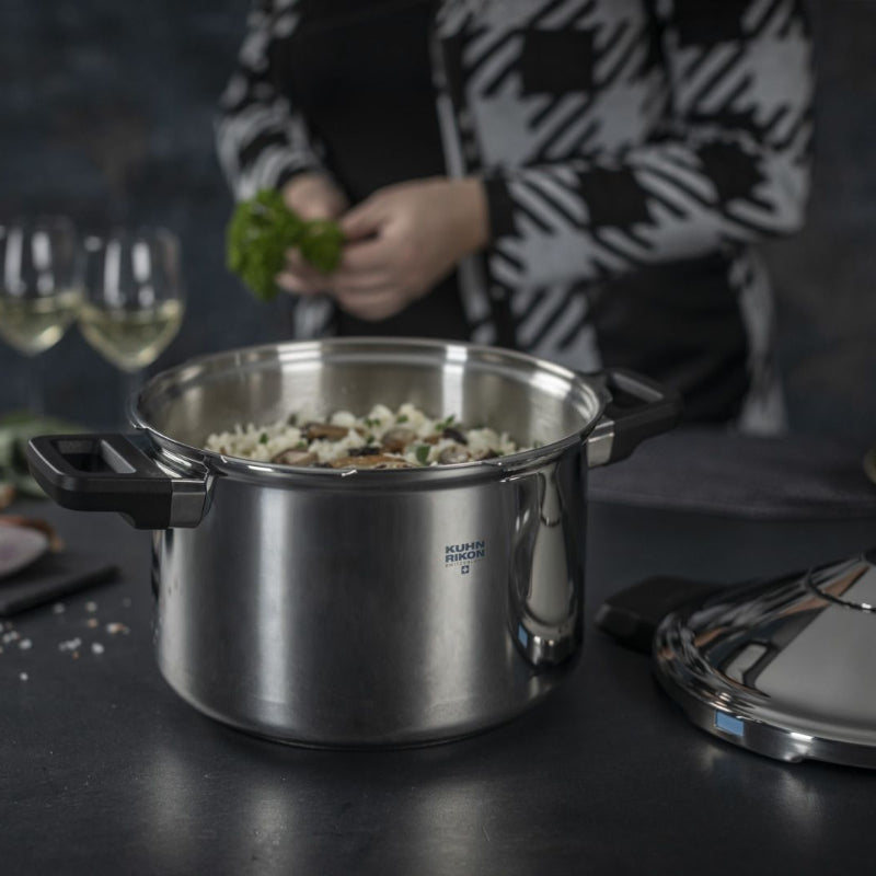 Stainless steel pot on a table with ingredients and a person in the background