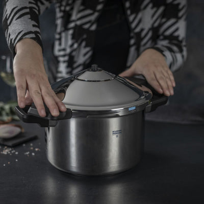 Person holding a pressure cooker on a dark surface with ingredients in the background