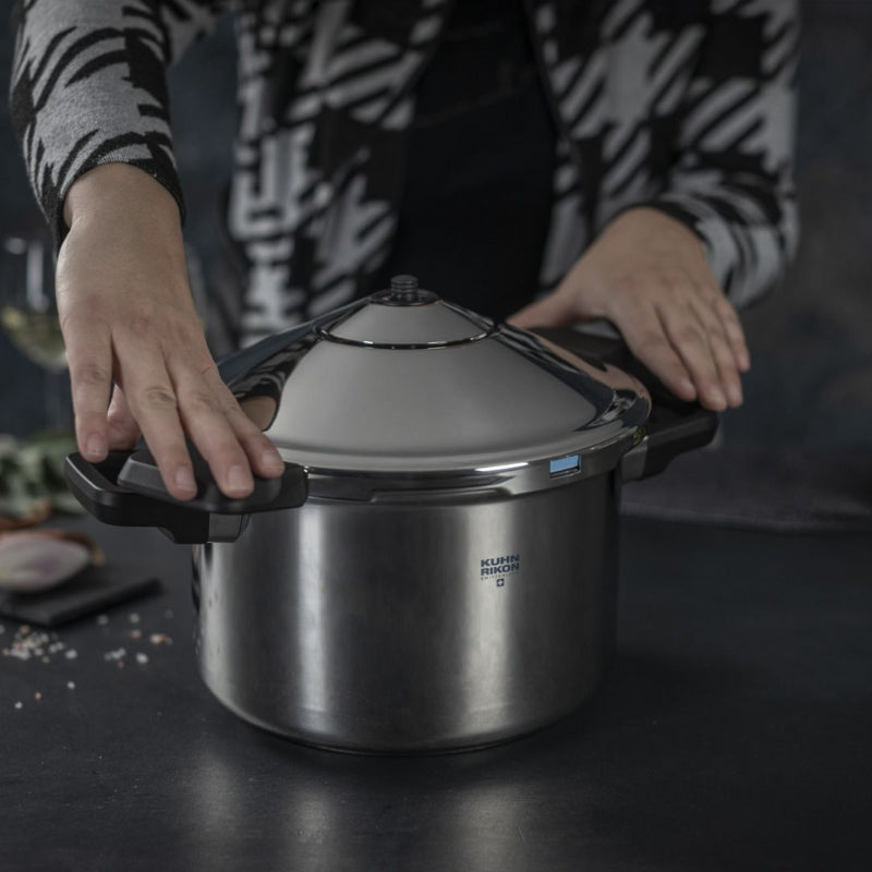 Person holding a pressure cooker on a dark surface with ingredients in the background