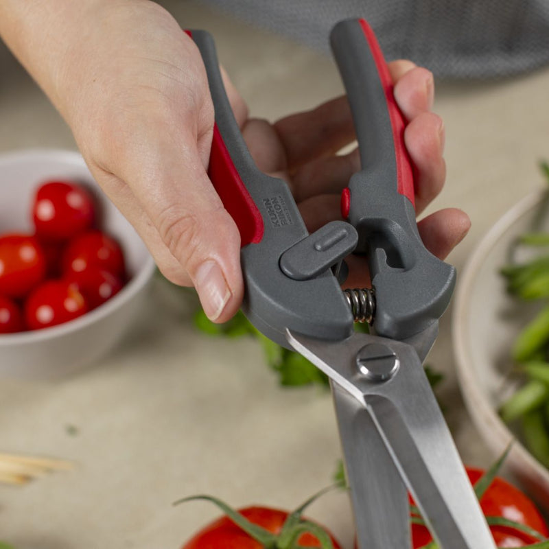 Hand using kitchen shears with a bowl of cherry tomatoes and green beans in the background.