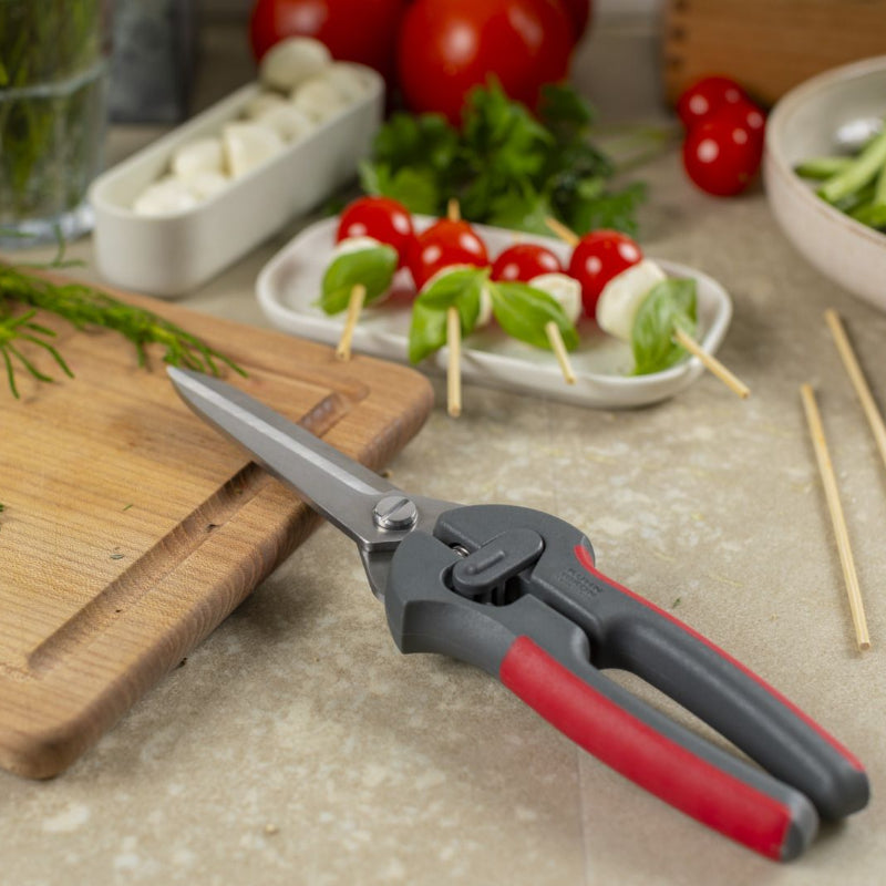 Pruning shears on a kitchen counter with vegetables and a cutting board in the background