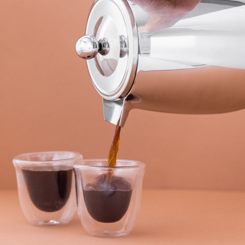 White French press pouring coffee into two clear cups on a beige background