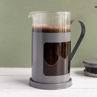 French press with coffee on a white surface and green background