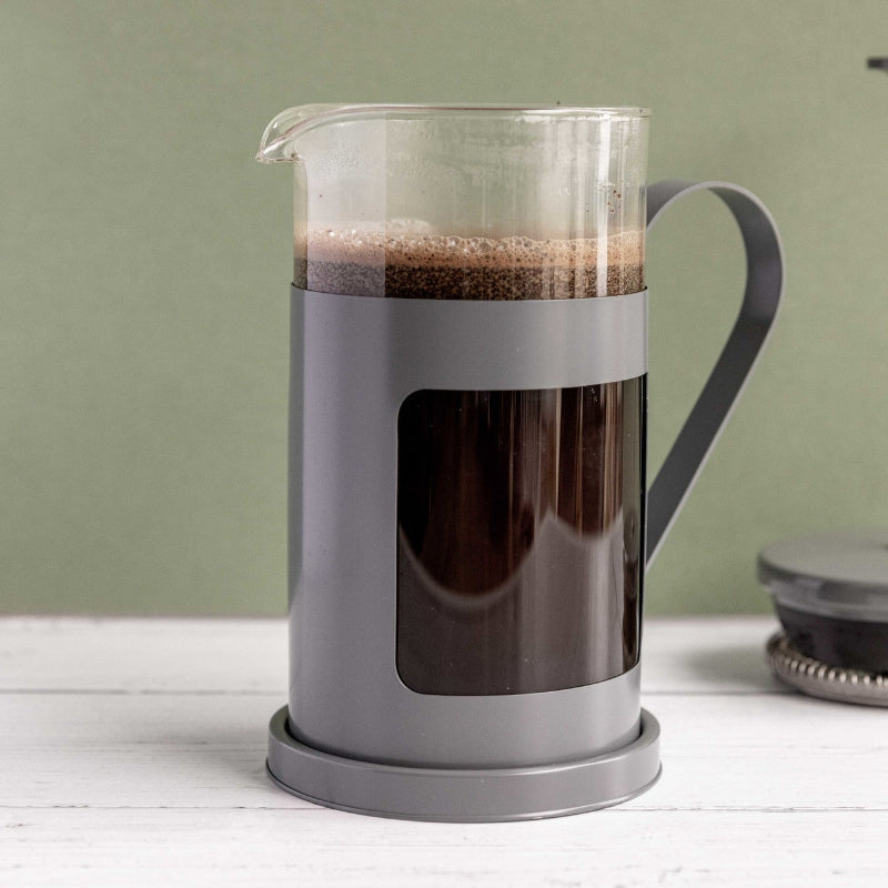 French press with coffee on a white surface and green background