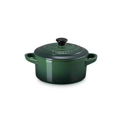 Green enameled cast iron cocotte with a black lid on a white background